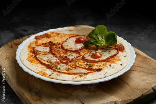 Close-up of Halloween-themed pizza with smiling face made from vegetables and cheese on white plate over wooden board, top view food photography