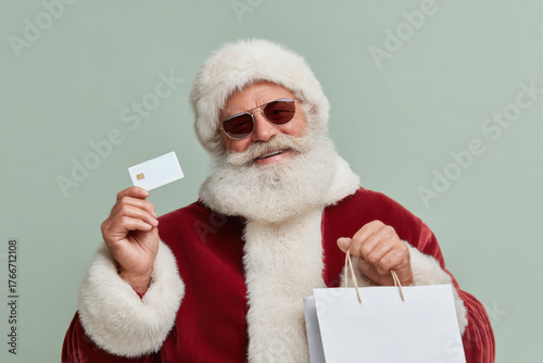 Santa Claus wearing sunglasses holds a shopping bag and a gift card at a festive location ready for holiday fun