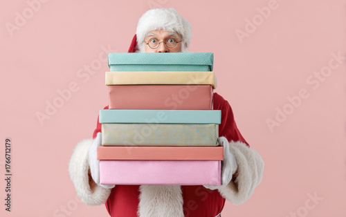 Santa Claus skillfully balances a stack of colorful gift boxes against a vibrant pink background