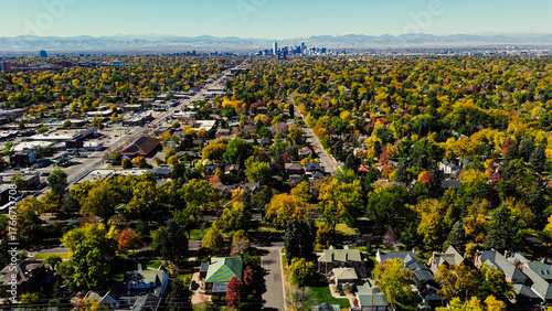 Large boulevard leading to downtown Denver and mountain backdrops from colorful suburban neighborhood framed in fall foliage blankets, mixed of single-family homes, commercial zones, retailers