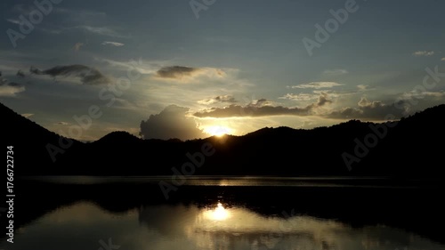 Time-lapse video of colorful clouds rolling over a lake, with a blue mountain range reflection