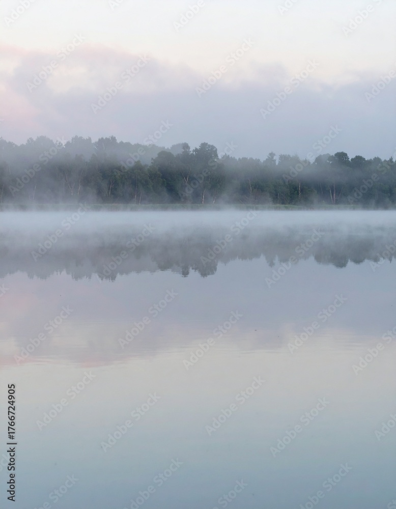 Fototapeta premium Soft mist over calm lake during sunrise showing peaceful natural reflection
