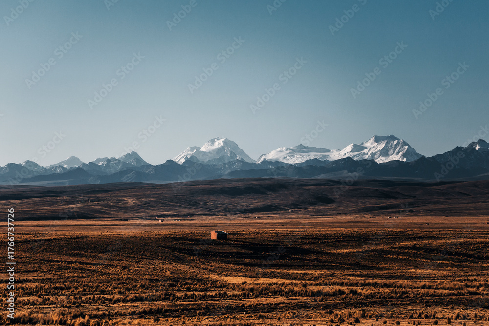 Obraz premium arid landscape in bolivia with snowy peaks in the background and a small house