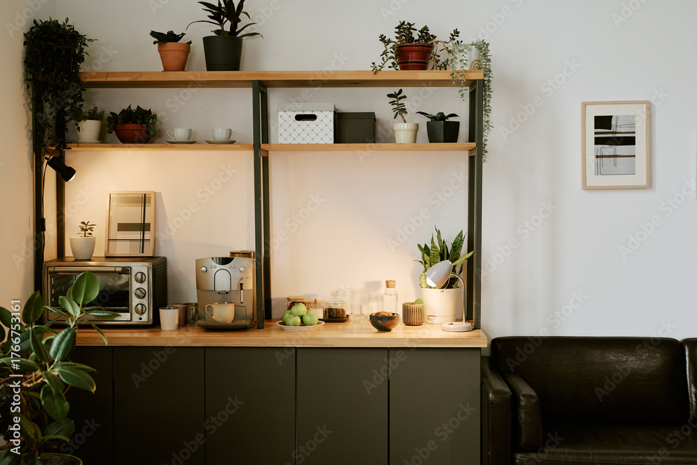 Fototapeta premium Modern kitchen counter featuring coffee machine, toaster oven, glass jars, fruit bowl, potted plants and lamp arranged on wooden shelves against wall with framed artwork