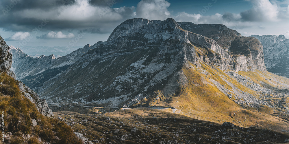 Naklejka premium Majestic mountain landscape in Durmitor National Park, Montenegro. Sunlight illuminating vast rocky slopes and a winding road