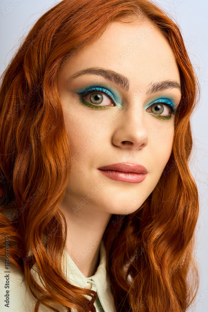 Naklejka premium A young redhead woman poses confidently, highlighting her vibrant makeup in a studio
