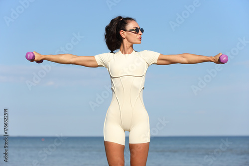 Fit woman exercising with dumbbells by the sea