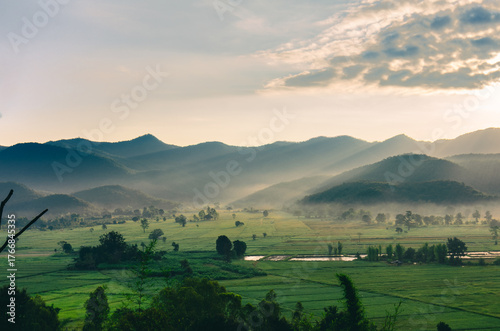 Beautiful view of morning light hitting mountains, green rice fields, trees, and mist in the countryside in Chiang Rai, Thailand.