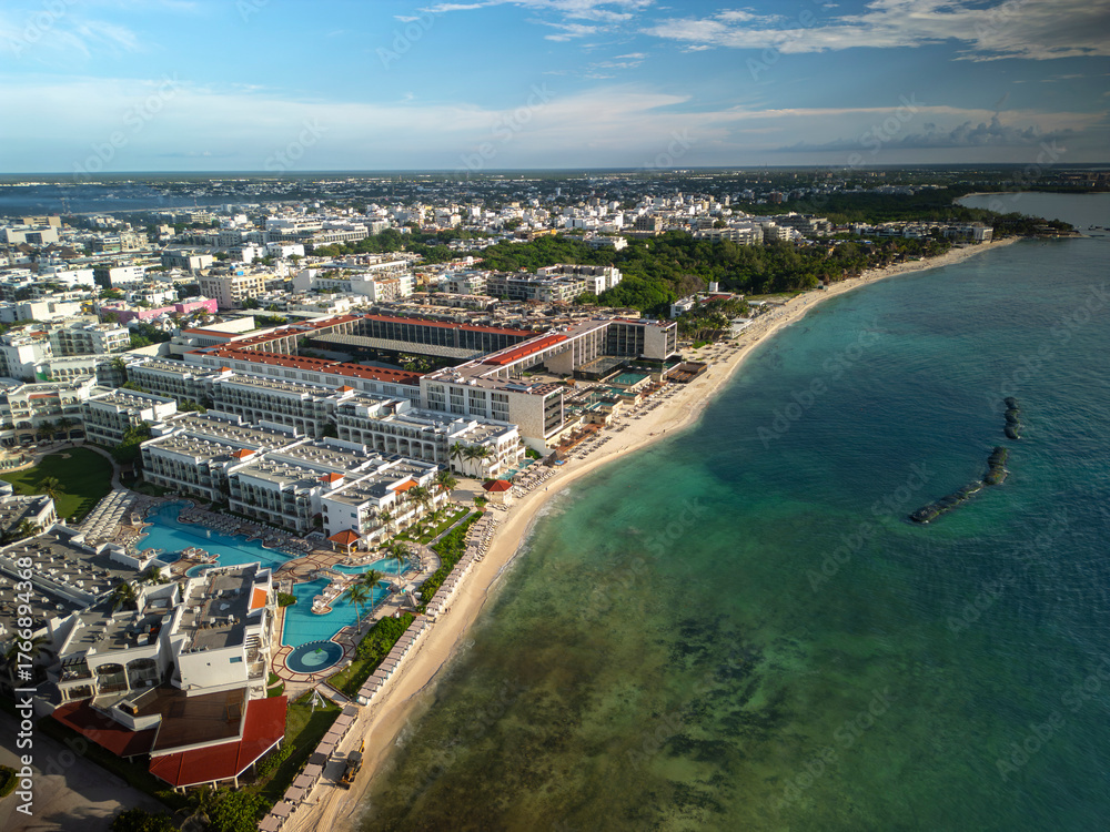 Obraz premium Aerial drone view of white sand beach, blue ocean, resorts, hotels, and a tourist town surrounded by lush green trees. Sunny day, blue sky. Playa del Carmen, Riviera Maya, Mexico.