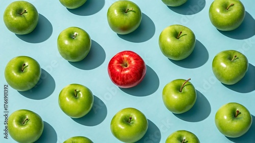 A single red apple stands out among many green apples on a blue background, symbolizing individuality, uniqueness, and thinking differently in a group