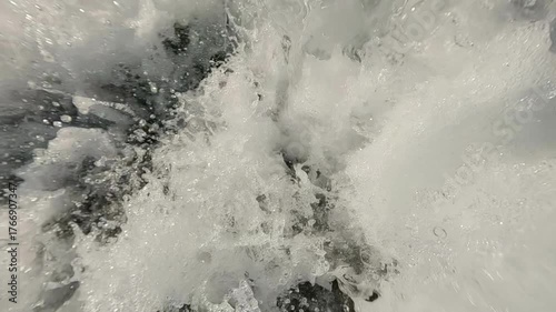 Extreme close-up of turbulent water flow from a waterfall with rushing and foaming water at shallow depths, with splashes flying in all directions, super slow motion.