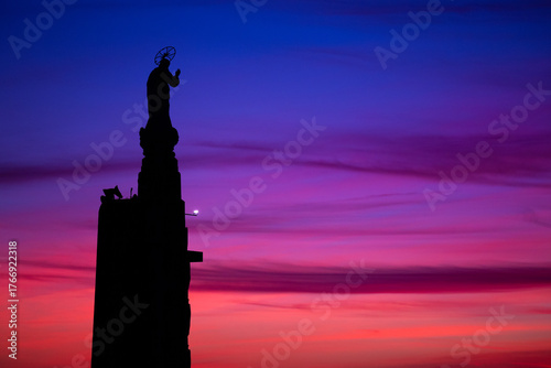 The silhouette of a religious statue stands against a winter sunset, where deep blues and soft pinks blend into violet. Sameiro Sanctuary, Braga, Portugal.