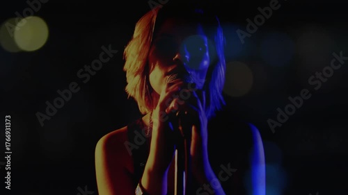 Teenage singer bringing microphone to lips and starting music performance under colored spotlights