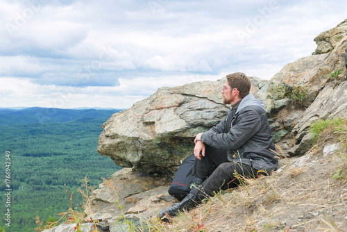 A man in a gray jacket is sitting on a mountain top.