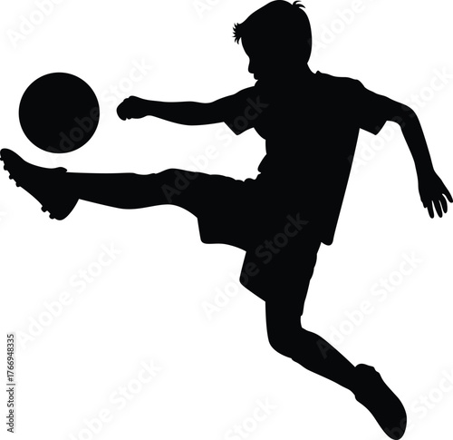 Silhouette of a young boy kicking a soccer ball in mid air during a game