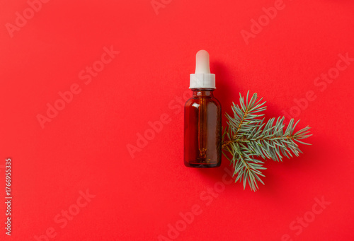 Fototapeta Cosmetic serum bottle with a pine twig on a red background