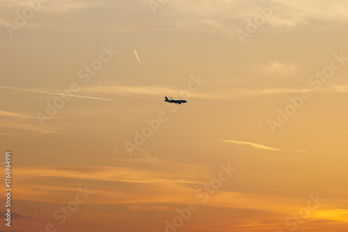 Airplane silhouette against a golden sunset sky with contrails