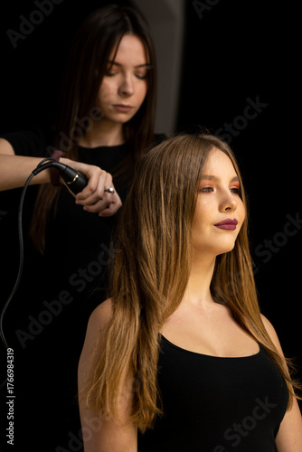 Tableau sur toile Hair stylist straightening long hair of young woman in beauty salon professional