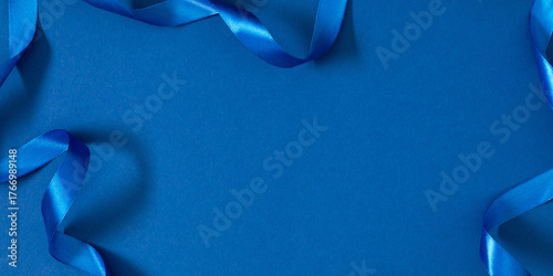 Blue satin ribbon on blue background. Minimal festive layout with copy space. Elegant background for greetings, advertising, invitations, or Christmas and New Year design.