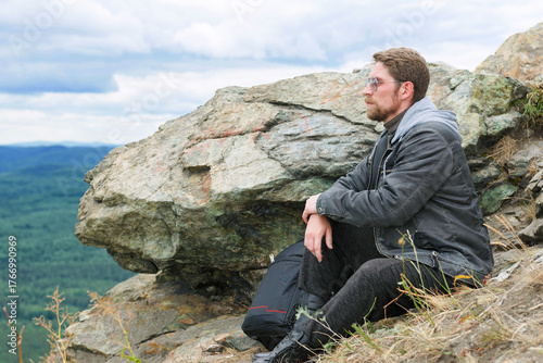 Man in a gray jacket is sitting on a mountain top.