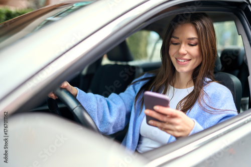Young happy woman driver sitting inside car holding smartphone using gps navigation map app on mobile phone looking at cellphone chacking traffic on city roads. Driving applications concept.