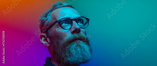 Stylish man in glasses with colorful neon lighting looking up.