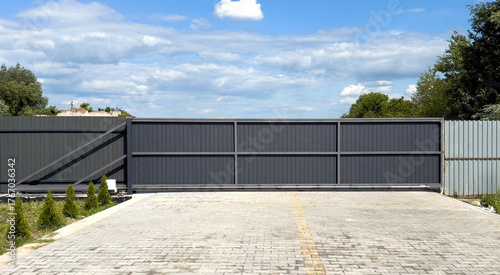 Dark gray metal sliding gate on paved driveway