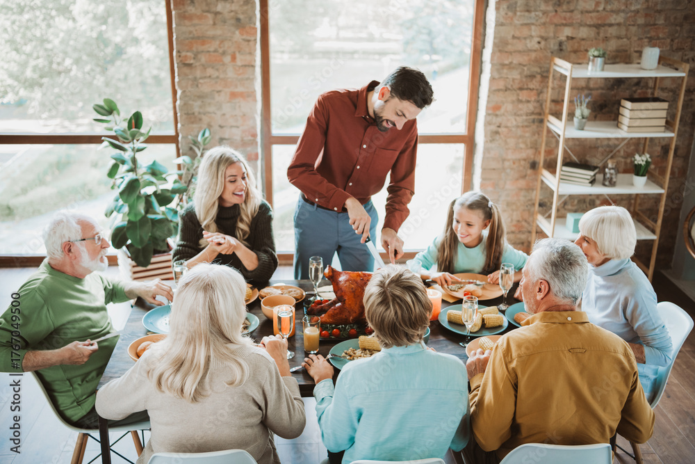 Fototapeta premium Joyful big family Thanksgiving feast around a long table with grandparents parents and kids sharing laughter food and love