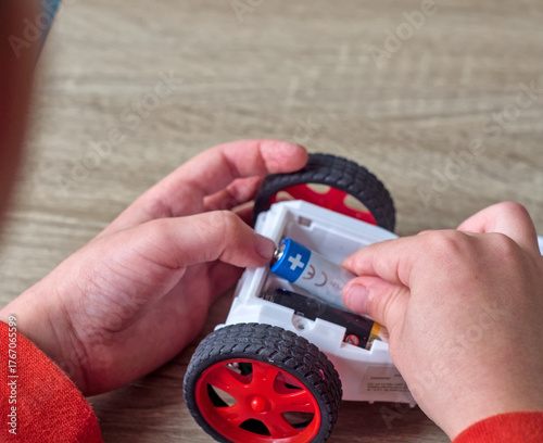 Installing Battery in Toy - A person's hands are shown installing or changing the batteries in a small toy car - inserting a AA battery