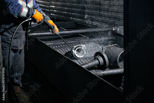 Industrial worker using high-pressure water jet to clean machinery parts in a workshop, showcasing the power of technology and dedication to maintenance tasks