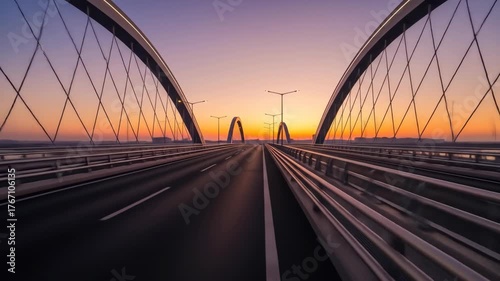 A scenic bridge at sunset with elegant arches and road lines under an orange and purple sky