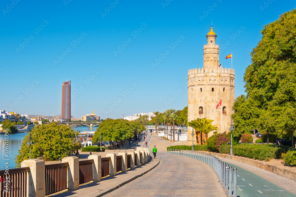 Fototapeta premium View from the waterfront promenade along the Guadalquivir River of the Torre del Oro Golden Tower and the Sevilla Tower in the distance, in Seville, Spain.