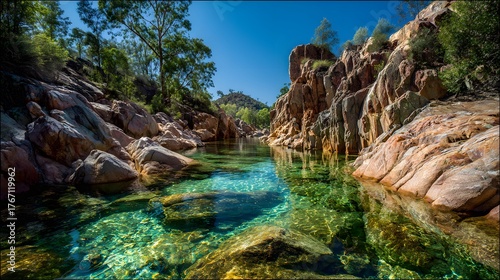 Deep emerald water flows between high rugged rock formations under a bright blue sky