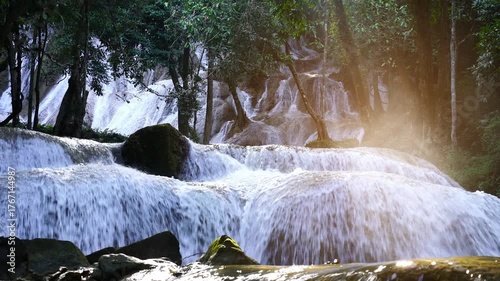 Tropical waterfall in lush forest illuminated by sunbeam, creating a magical and tranquil atmosphere. Perfect for nature inspiration, wellness visuals, eco-tourism, and meditation content.