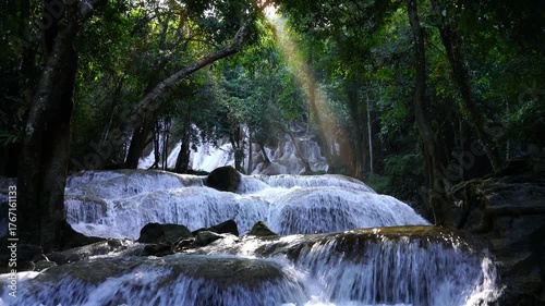 Tropical waterfall in lush forest illuminated by sunbeam, creating a magical and tranquil atmosphere. Perfect for nature inspiration, wellness visuals, eco-tourism, and meditation content.
