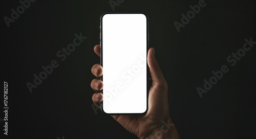 Smartphone Display in Hand: A close-up shot of a hand holding a modern smartphone with a blank, bright screen, providing ample space for digital content or app display against a stark, dark backdrop.