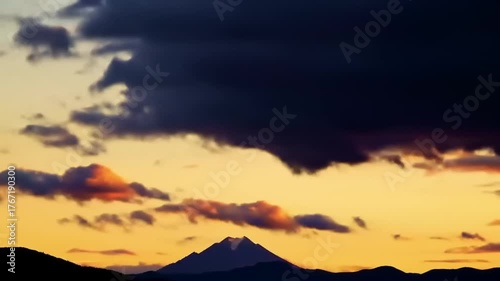 Dramatic sunset over mountain silhouette with fluffy clouds and golden light