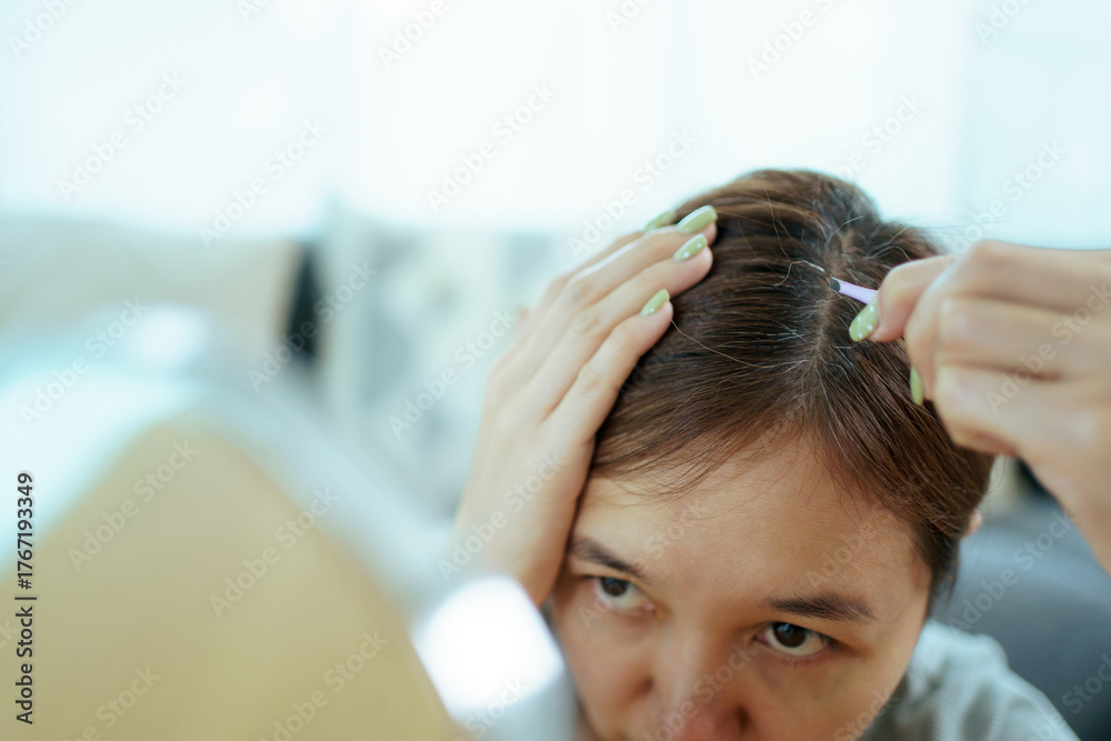 Fototapeta premium Asian woman removing gray hair with tweezers at home