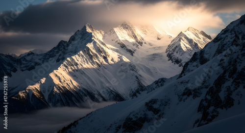 Snowy mountain peaks under dramatic clouds illuminated by sunlight in winter