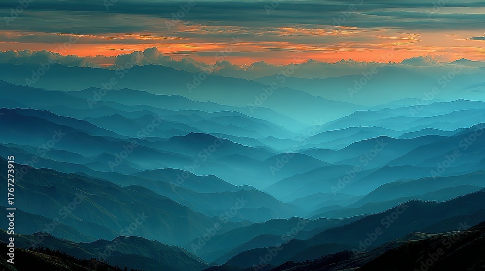 Obraz premium Mountain range landscape with blue hues and an orange sky at the horizon.