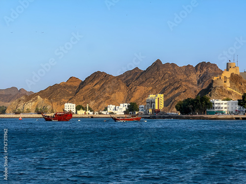 Coastal view of Muscat city and rocky mountains. Beautiful seascape showing the coast of Muscat, Oman with rugged mountains and clear blue waters.

