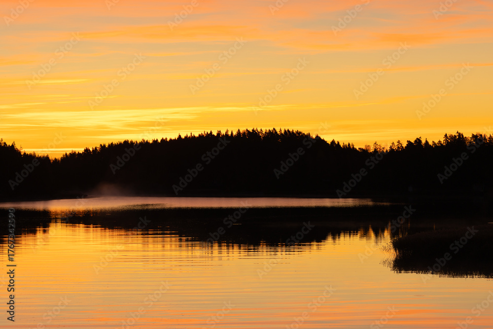Fototapeta premium Golden sunrise over calm autumn sea with forest on the shore and gentle fog above the water, peaceful natural seascape and morning atmosphere