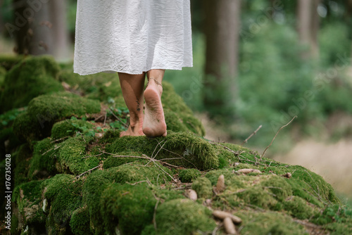 Feet of a barefoot woman walking slowly over moss in the forest, close-up of natural movement