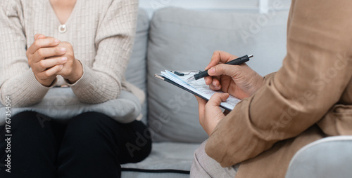 Close-up of psychologist hand writing, taking note about patient, listening to patient at psychotherapy session in office. Professional Psychologist consult with clipboard during treatment interview.
