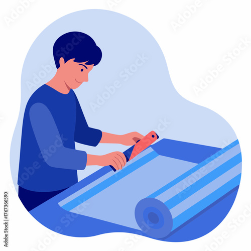 Young man cutting wallpaper roll with stationery knife at workstation  