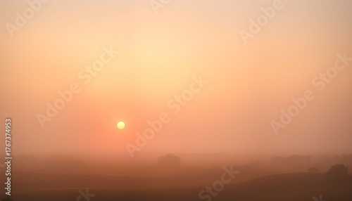 A serene sunrise illuminates a hazy landscape, creating an ethereal and warm atmosphere.