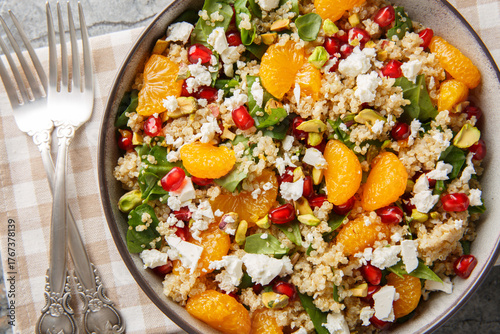 Pomegranate and Orange Quinoa Salad with added spinach,  feta and crispy pistachios closeup on the plate on the table. Horizontal top view from above