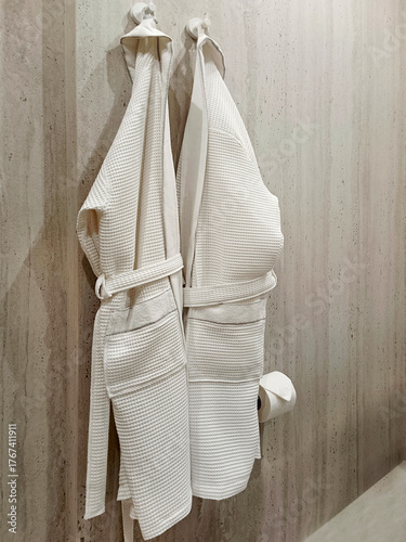 White bathrobes hanging on a hook in the bathroom. Close-up, vertical photo.