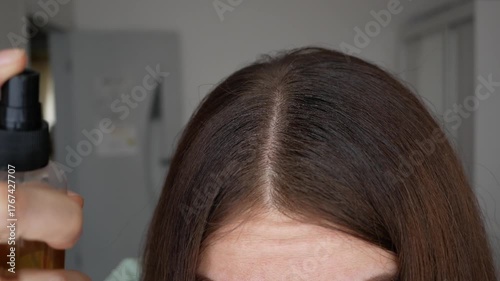 Woman applying a hair growth product to her scalp. Anti-hair loss spray. A procedure to restore hair growth