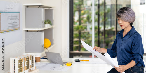 Professional construction engineer checking details on blueprint in construction site office.